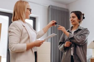 A real estate agent handing keys to a smiling client, symbolizing a successful home sale. Perfect for illustrating “What is a broker open” and how these events help connect agents with potential buyers.
